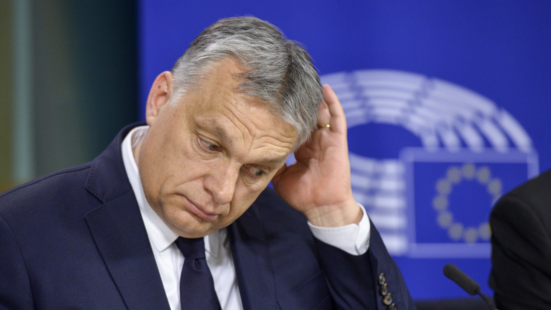 Viktor Orban looking defeated with a European Parliament logo behind him