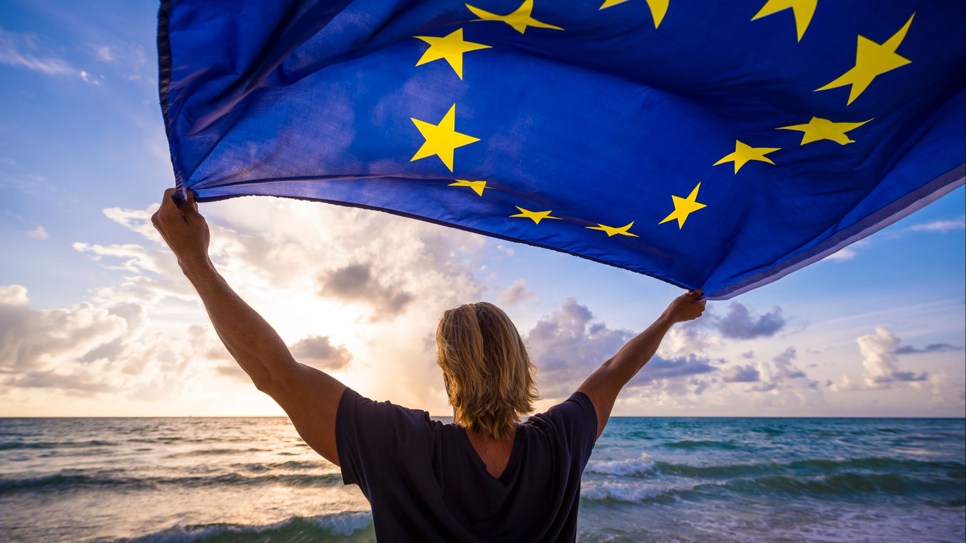 Woman holding EU flag above her head looking towards horizon